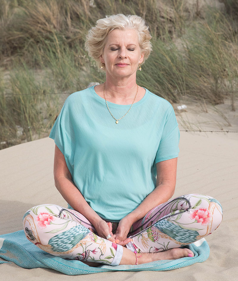 Karin de Jong, HSP-coach bij praktijk Kracht in Gevoel, mediterend op een zandduin, straalt rust en zelfreflectie uit.