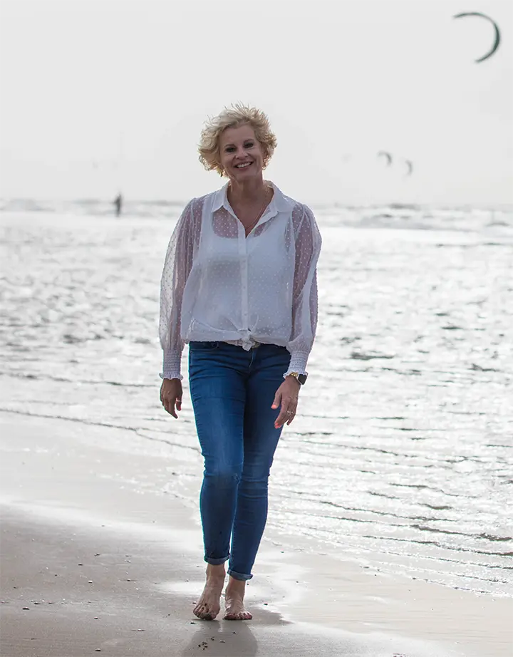 Vrouw wandelt ontspannen op het strand, symbolisch voor rust en balans bij integrale coaching voor hoogsensitieve personen (HSP).